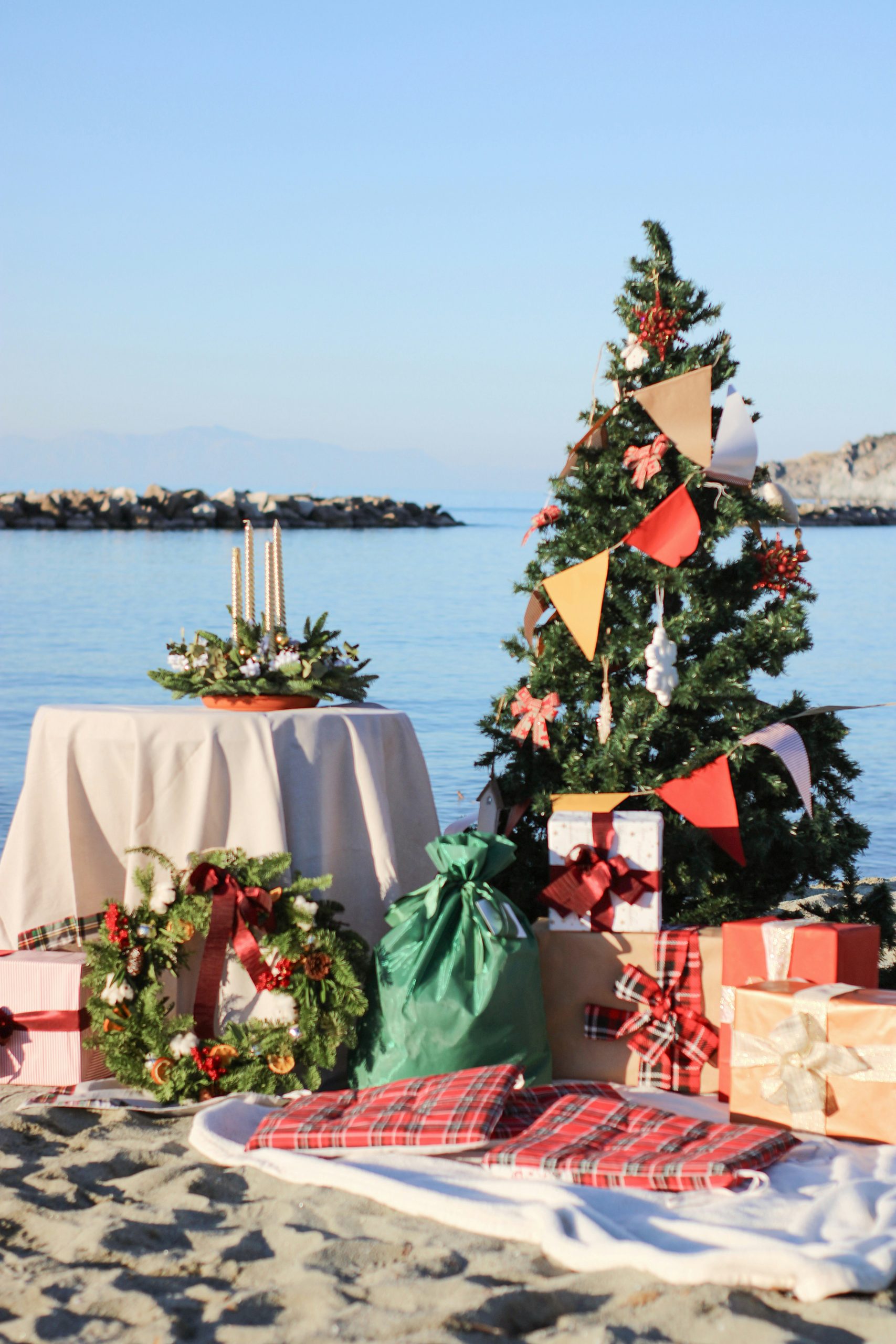 Festeggiamenti natalizi in riva al mare con un albero di Natale in spiaggia, decorazioni e regali, perfetto per chi sogna un Natale al caldo con un tocco di magia grazie al Babbo Natale estivo