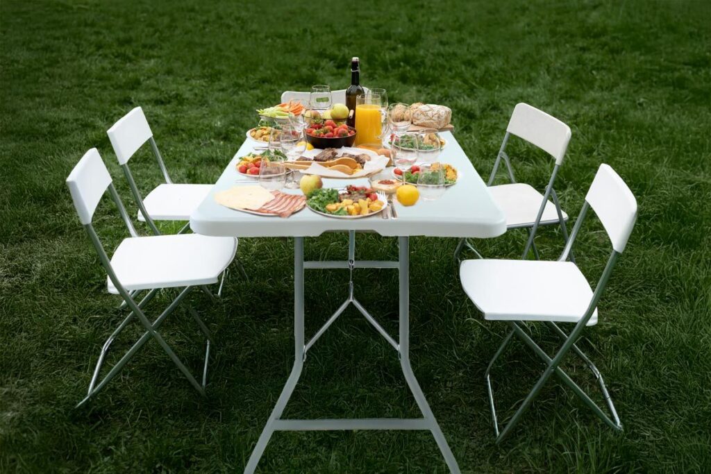 Tavolo pieghevole posizionato su prato in giardino, apparecchiato per un pranzo all’aperto