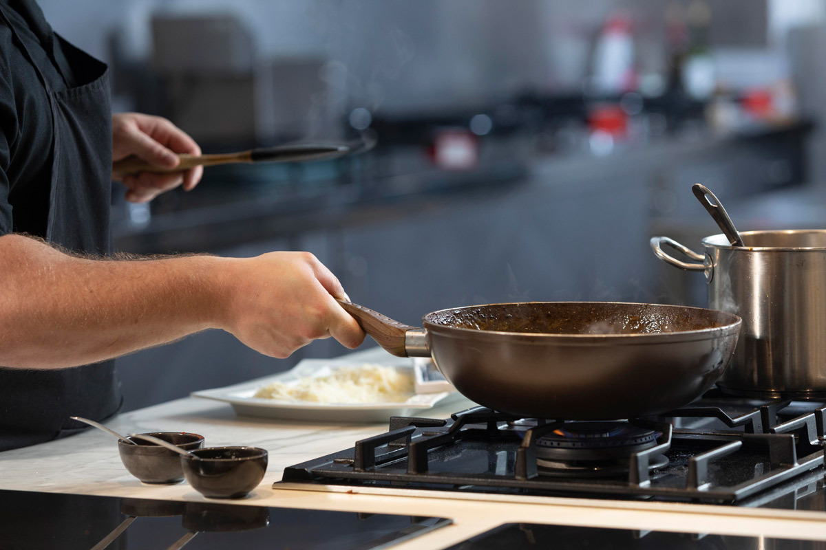Chef professionista che cucina con pentole in acciaio e ghisa su fornelli professionali