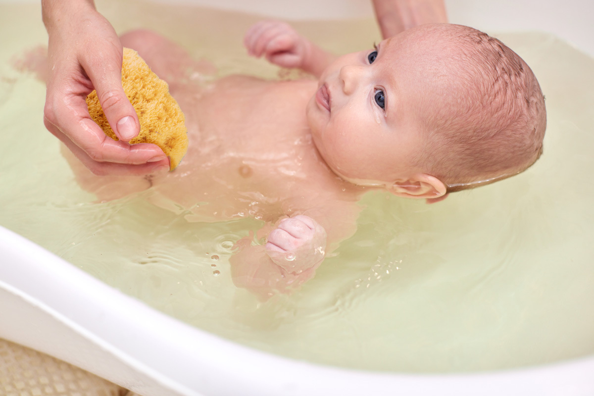 Mamma che fa il bagnetto a un neonato con bagnoschiuma naturale e spugna morbida