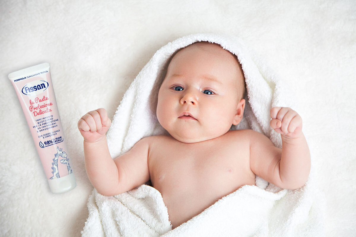 Neonato avvolto in asciugamano dopo il bagnetto con crema idratante sul fasciatoio